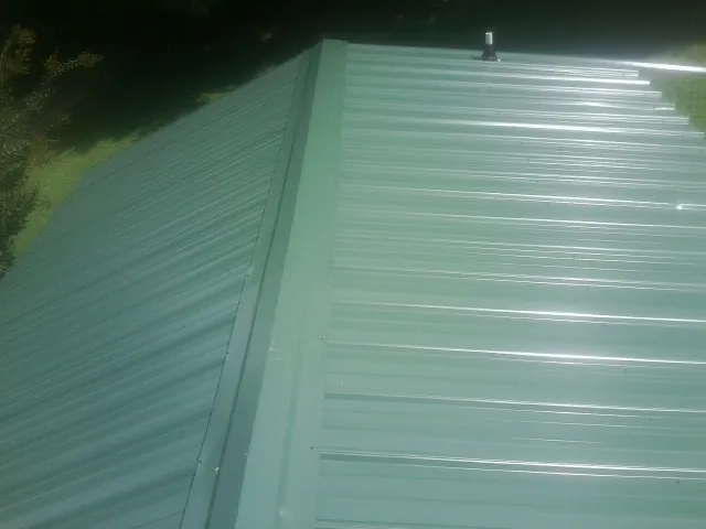 New green metal panels meeting at the ridge of a roof — Flat Roof Repair work by our crew in Middlesboro