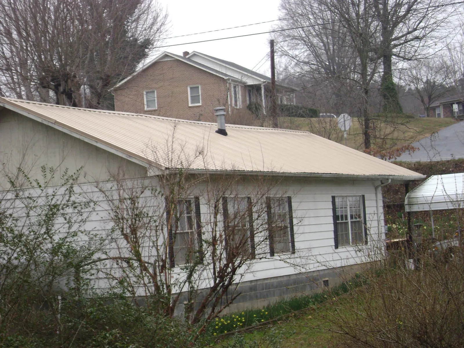 Tan metal roof on a white sided house set into a hillside — Commercial Roofing by Roofing Brothers in Middlesboro